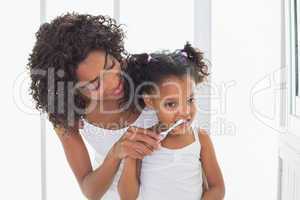 Pretty mother helping her daughter brush her teeth