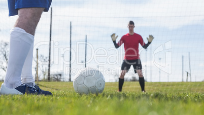 Goalkeeper in red waiting for striker to hit ball