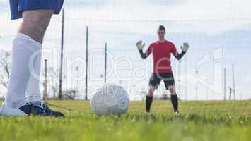 Goalkeeper in red waiting for striker to hit ball