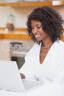 Pretty woman in bathrobe using laptop at table