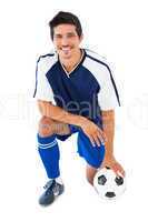 Football player in blue kneeling with ball