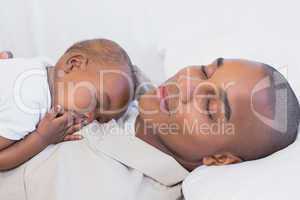 Happy young father napping with baby son on couch