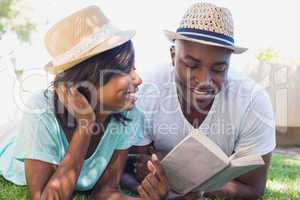 Happy couple lying in garden together reading book