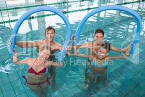 Happy fitness class doing aqua aerobics with foam rollers