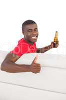 Football fan in red jersey sitting on couch holding beer showing
