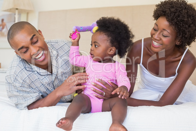 Happy parents playing with baby girl on bed together