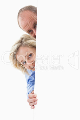 Mature couple smiling behind wall