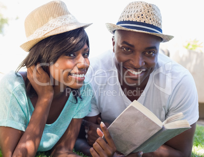 Happy couple lying in garden together reading book