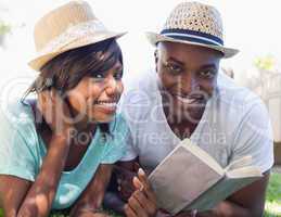 Happy couple lying in garden together reading book