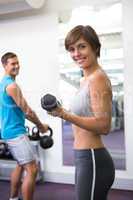 Fit couple lifting weights together smiling at camera