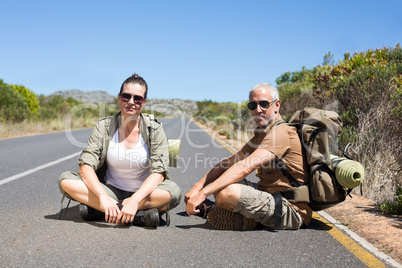Hitch hiking couple sitting on the side of the road looking at c
