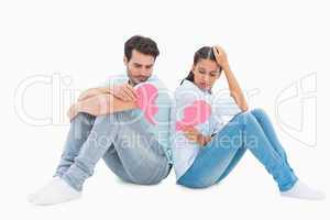 Sad couple sitting holding two halves of broken heart