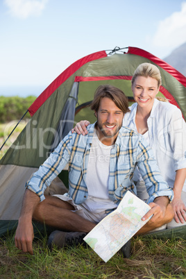 Attractive happy couple sitting by their tent smiling at camera