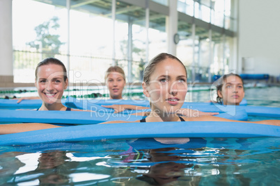 Female fitness class doing aqua aerobics with foam rollers