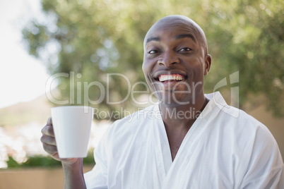 Handsome man in bathrobe having coffee outside