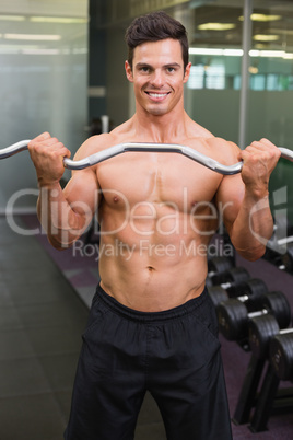 Smiling shirtless muscular man lifting barbell in gym