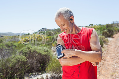 Fit man changing the song on his music player on mountain trail