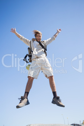 Handsome hiker jumping at the summit smiling at camera