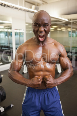 Muscular man shouting while flexing muscles in gym