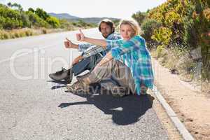 Attractive couple sitting on the road hitching a lift