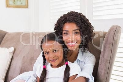 Pretty mother sitting on the couch with her daughter smiling at