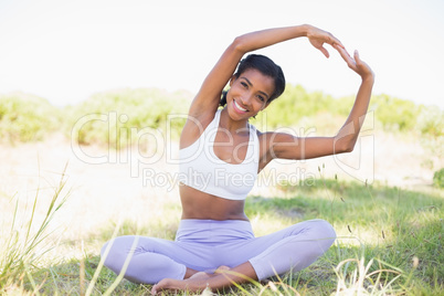 Fit woman sitting on grass in lotus pose smiling at camera