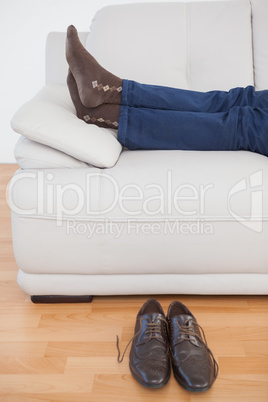 Tired businessman lying on sofa with shoes off