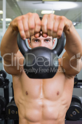 Muscular man lifting kettle bell in gym