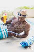 Handsome shirtless man using tablet pc poolside with cocktail