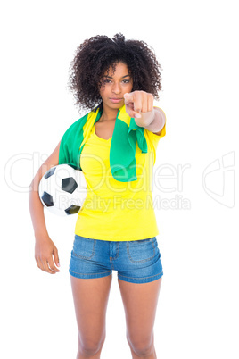 Pretty football fan holding brazilian flag pointing at camera