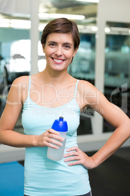 Fit brunette smiling at camera holding water bottle