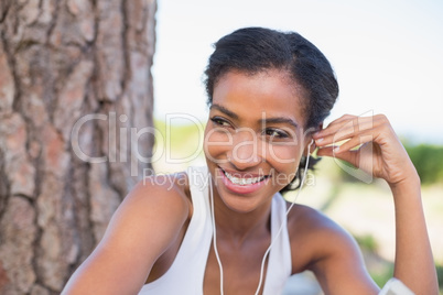 Fit woman sitting against tree listening to music