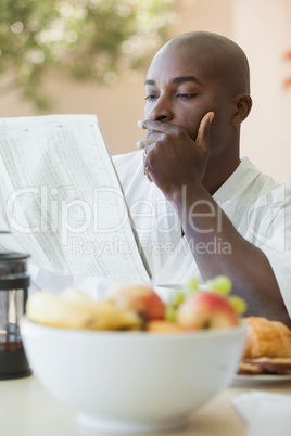 Man in bathrobe reading paper and having breakfast on terrace