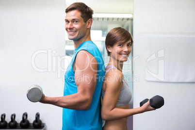 Fit couple lifting dumbbells together smiling at camera