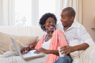 Cute couple relaxing on couch with laptop and coffee