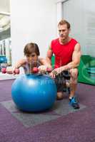 Personal trainer with client lifting dumbbells on exercise ball