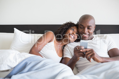 Happy couple cuddling in bed with smartphone