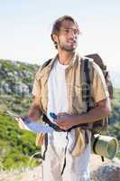 Handsome hiker holding map and compass at mountain summit