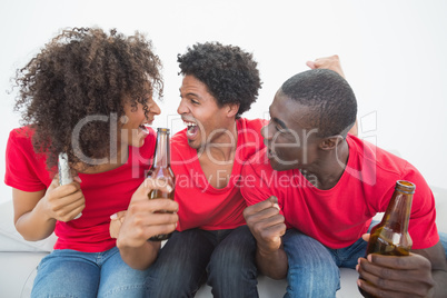 Football fans in red sitting on couch with beer cheering