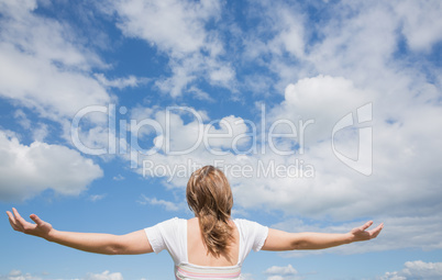 Woman with arms outstretched against blue sky and clouds