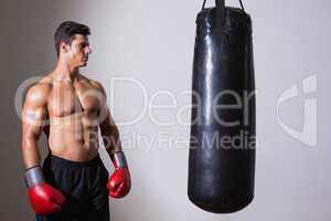 Shirtless muscular boxer looking at punching bag