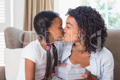 Pretty mother sitting on couch offering daughter a gift