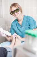 Smiling cosmetician working with laser to treat feet