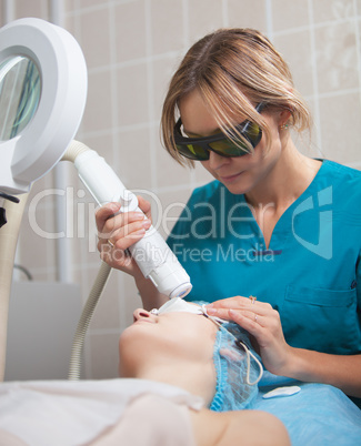 Cosmetician providing facial treatment with a laser