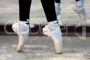 Close up view to ballerinas legs in pointes on wooden floor