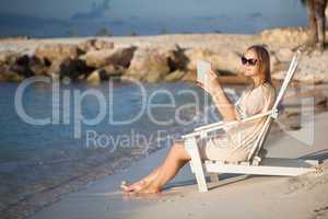 Woman with pad relaxing in chaise-lounge on the beach