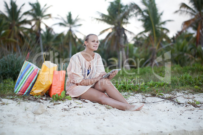 Woman relaxing with pad on beach after shopping