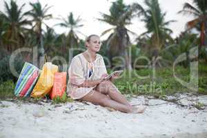 Woman relaxing with pad on beach after shopping