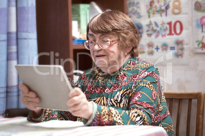 Elderly woman in glasses watching something on pad