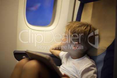 Boy in plane looking out illuminator with pad on lap